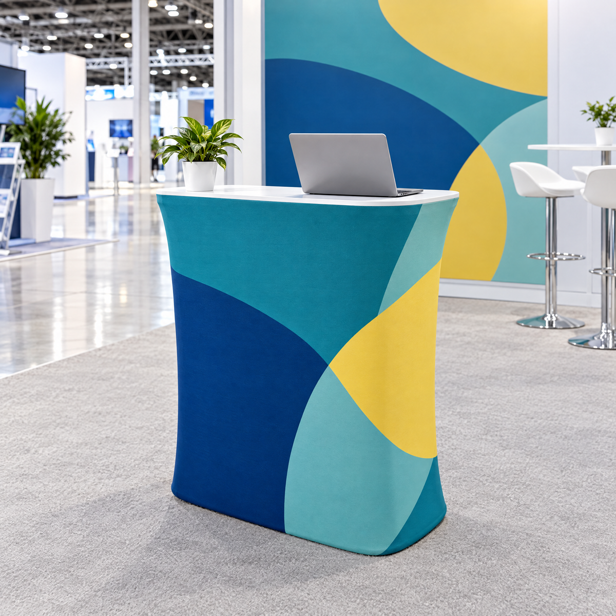 Desk textil drept la un stand de expoziție, folosit ca birou de informații, cu print abstract turcoaz, albastru și galben, un laptop și o plantă deasupra (imagine generată cu AI)